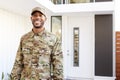 Millennial soldier in camouflage uniform standing outside modern house smiling to camera, close up Royalty Free Stock Photo