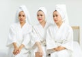 Millennial three Asian female customers friends in white clean bathrobes and towels have appointment at massage resort sitting on