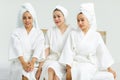 Millennial three Asian female customers friends in white clean bathrobes and towels have appointment at massage resort sitting on