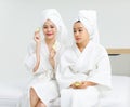 Millennial two Asian female customers friends in white clean bathrobes and towels have appointment at massage resort sitting on