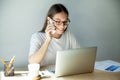 Millennial woman in glasses talking on mobile and using laptop