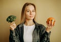 millennial woman show broccoli and orange. Sports, weight loss and body care, choice of harmful and healthy food