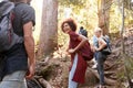 Millennials hiking up a forest trail turning around to look back at friends, three quarter length