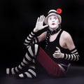 Mime in white hat with red flower sits on the floor