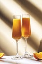 Mimosa alcohol cocktail drink with orange juice and cold dry champagne or sparkling wine in glasses. Beige background, hard light