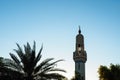 Minaret of mosque and silhouette of date palm on blue sky background in sunny day, copy space Royalty Free Stock Photo