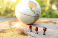 Minature people: traveling with a backpack standing on vintage world map and globe, Travel and vacation concept