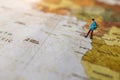 Minature people: traveling with a backpack standing on vintage world map.