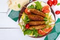 Minced meat on skewers - lula kebabs on a plate with fresh vegetables and greens on a white background. Royalty Free Stock Photo