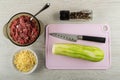 Minced meat, spoon in bowl, bowl with grated cheese, condiment, knife, peeled squash on cutting board on wooden table. Top view