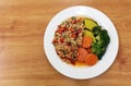 Minced pork spicy salad in white plate eat with chili, carrot, pumpkin, broccoli and vegetables, isolated in wooden table. Royalty Free Stock Photo