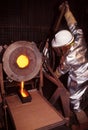 Mine worker wearing heat protective clothing and mask pours molten Gold into ingot mold