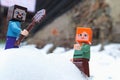 Minecraft LEGO figures of Steve and Alex standing on snow, building detail in background