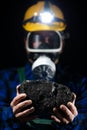 A miner in a helmet with a glowing flashlight and a dust mask on holds a large lump of coal in his hands Royalty Free Stock Photo