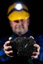 A miner holds a large lump of coal in his hands. A helmet with a lit flashlight on the miner& x27;s head Royalty Free Stock Photo