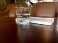 Mineral drink water in transparent glass with notebook on brown wooden table.