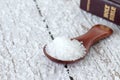 Mineral salt in a wooden spoon with closed holy bible book on table, close-up