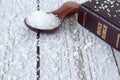 Mineral salt in a wooden spoon with closed holy bible book on table