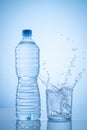 Mineral water bottle and water glass  with spash on blue background with copy space. Vertical format Royalty Free Stock Photo