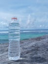 mineral water in a plastic bottle on a wooden table, with a beach background and beautiful white clouds in the sky Royalty Free Stock Photo