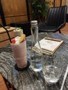 Mineral water, strawberry cheese cake drink, table texture natural stone, menu book, black chair