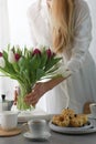 Mini bundt cakes with fruits on plate, cup of coffee and girl put bouquet of tulip flowers in a vase. Royalty Free Stock Photo