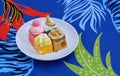 Various mini cakes in white dish on colorful foliage pattern of tablecloth Royalty Free Stock Photo