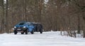 Mini camper on winter forest road towed by blue muscle car. Caravan or recreational vehicle motor home trailer on a