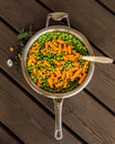 Mini carrots with green peas in a metal pan on a wooden background. the view from the top