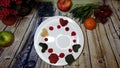 Mini colorful pancakes placed arround a white plate on a wooden background surrounded by fruits