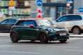 Mini Cooper fast driving on the street. Green small city car in blurred motion, front side view