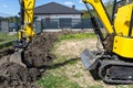 Mini digger digging a hole in the garden along the fence to the drainage pipes.