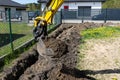 Mini digger digging a hole in the garden along the fence to the drainage pipes.