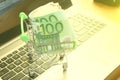 mini dummy shopping cart on laptop with paper euro banknotes as a concept for online shopping, saving, business and making money a