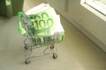 mini dummy shopping cart in human hand with paper euro banknotes as a concept for online shopping, saving, business and making mon