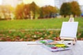 Mini easel, paint and brush on the background of the city park. Draw a landscape in city park. Artist and painting concept. Royalty Free Stock Photo