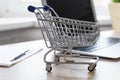 Mini empty shop cart trolley over a laptop computer on wood table background