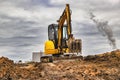 Mini excavator at the construction site on the edge of a pit against a cloudy blue sky. Compact construction equipment for Royalty Free Stock Photo