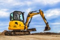 Mini excavator at the construction site on the edge of a pit against a cloudy blue sky. Compact construction equipment for Royalty Free Stock Photo