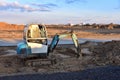 Mini excavator digg trench to lay cables concrete curbs and paving slabs at construction site. Backhoe on earthwork/roadworks