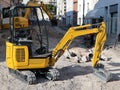 A mini excavator with a large excavator behind it at work in the renovation of the road surface