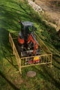 Mini excavator surrounded by fence above ground in a field or forest.