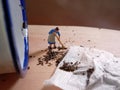 Photo Mini figure toy woman cleaning spilled tea at wooden board beyond small white aluminium glass