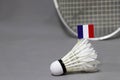 Mini France flag stick on the white shuttlecock on the grey background and out focus badminton racket