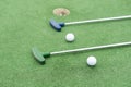 Mini-golf clubs and balls of different colors laid on artificial grass