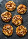Mini ham, tomato sauce, mozzarella, sun dried tomatoes pizza on a dark background, top view. Delicious breakfast, snack, tapas