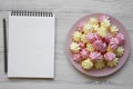 Mini meringues on pink plate and blank notepad on a white wooden background, top view. Close-up. Space for text