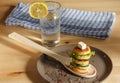 Mini pancakes on a wooden spoon ,a glass of water with lemon and a checkered napkin on a wooden table