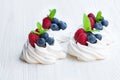 Mini Pavlova meringue cakes with berries and mint on white wood