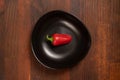 Mini red bell pepper laying in a black bawl isolated on wooden background. Top view Royalty Free Stock Photo